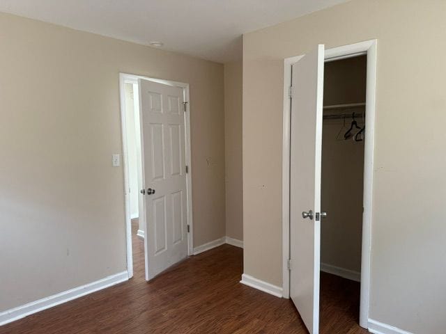 unfurnished bedroom with baseboards, a spacious closet, wood finished floors, and a closet