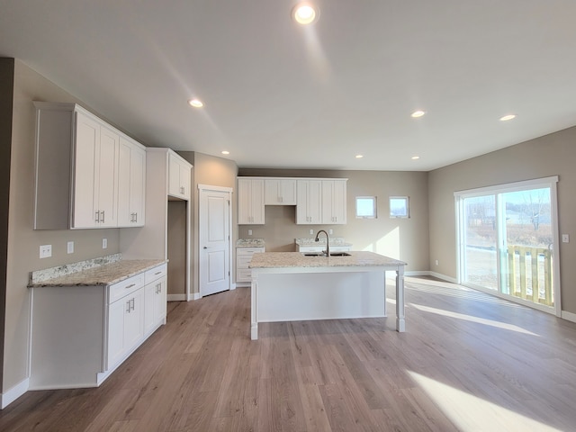 kitchen featuring white cabinets, a sink, light wood-style floors, baseboards, and a kitchen island with sink