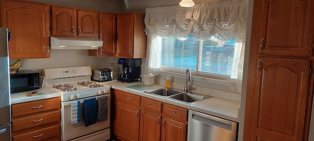 kitchen featuring gas range gas stove, brown cabinetry, under cabinet range hood, dishwasher, and a sink