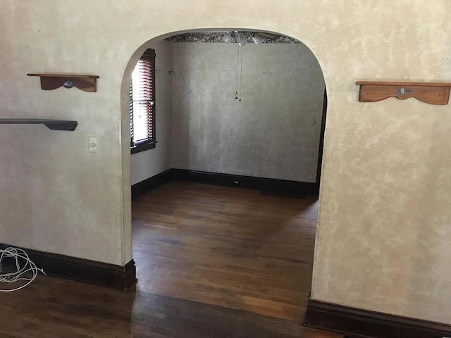 spare room with dark wood-type flooring, baseboards, and arched walkways