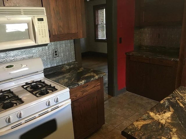 kitchen with white appliances, dark tile patterned flooring, and backsplash