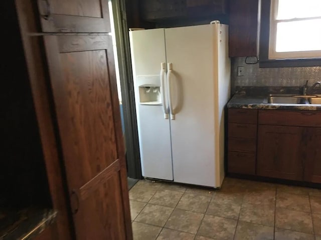 kitchen featuring dark countertops, light tile patterned floors, white fridge with ice dispenser, and a sink
