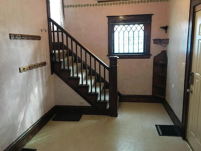 foyer entrance featuring baseboards, visible vents, tile patterned floors, and stairway