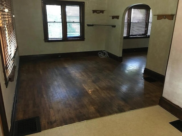 empty room with baseboards, visible vents, arched walkways, and wood-type flooring
