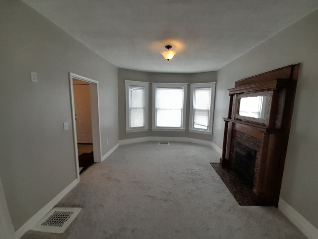 unfurnished living room with carpet floors, visible vents, and a fireplace with flush hearth