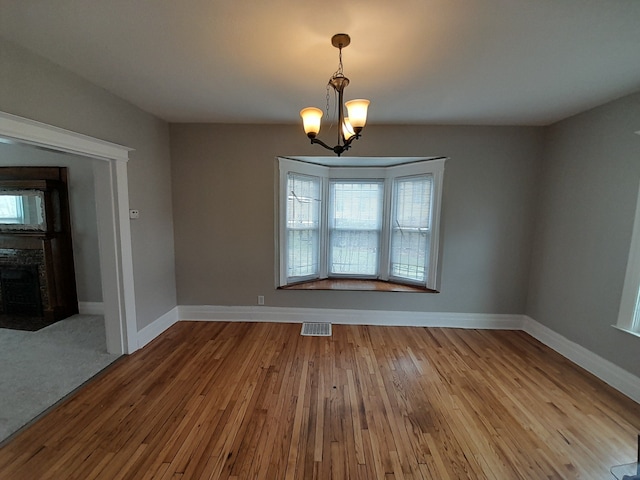 unfurnished dining area featuring visible vents, baseboards, a chandelier, and hardwood / wood-style flooring
