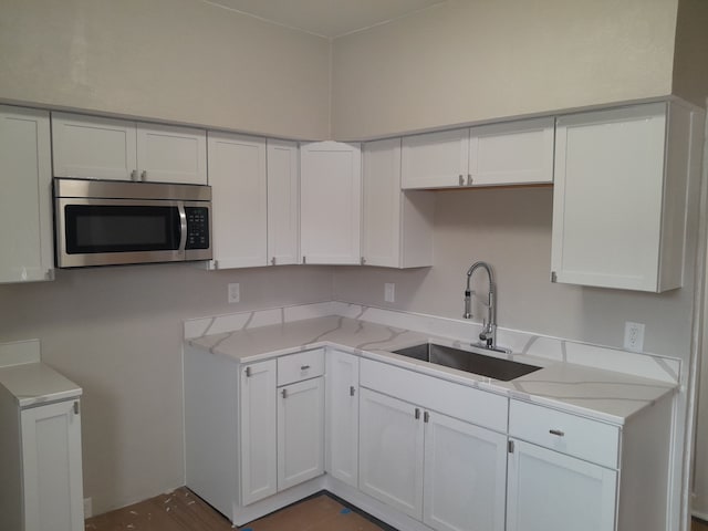 kitchen featuring white cabinetry, stainless steel microwave, light stone counters, and a sink
