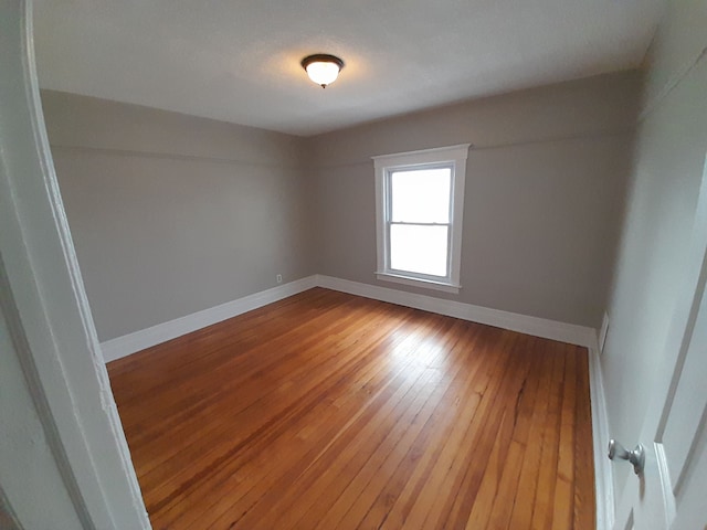 spare room featuring wood-type flooring and baseboards