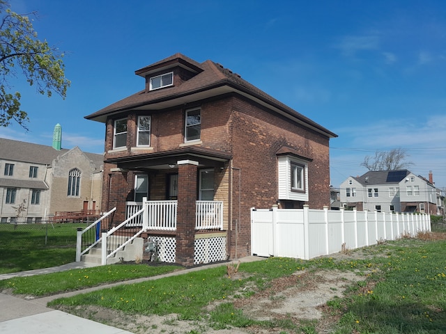 american foursquare style home featuring covered porch, brick siding, fence, and a front lawn