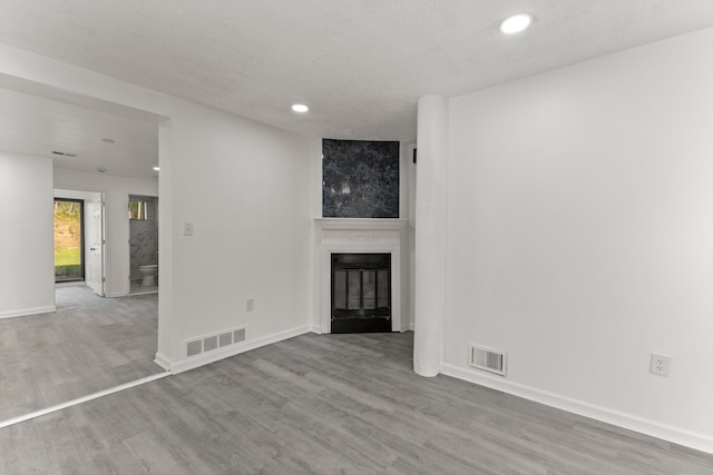 unfurnished living room featuring recessed lighting, visible vents, wood finished floors, and a glass covered fireplace