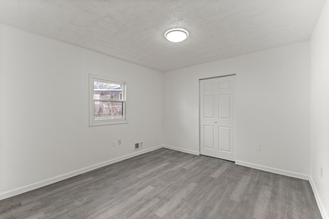 spare room with a textured ceiling, visible vents, wood finished floors, and baseboards