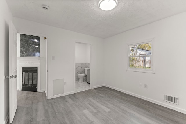 unfurnished bedroom with wood finished floors, a large fireplace, baseboards, visible vents, and a textured ceiling