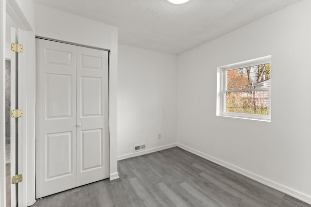 unfurnished bedroom featuring a closet, visible vents, wood finished floors, and baseboards