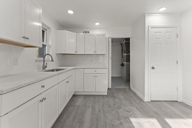 kitchen featuring baseboards, tasteful backsplash, light wood-style floors, a sink, and white cabinetry