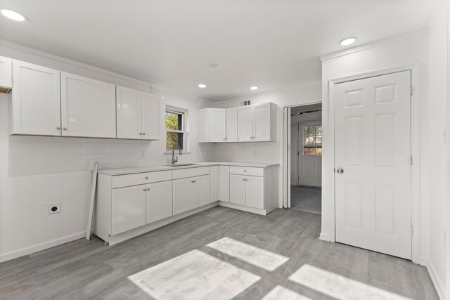 kitchen featuring light countertops, white cabinets, backsplash, light wood finished floors, and a sink