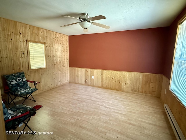 unfurnished room featuring wood walls, plenty of natural light, light wood-style flooring, and a baseboard radiator