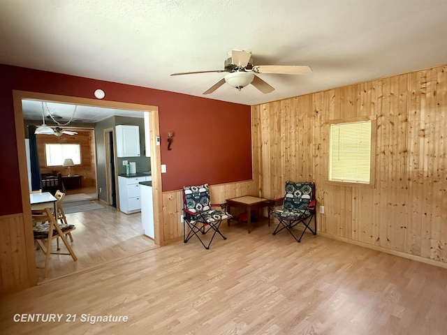 sitting room with wood walls, wood finished floors, ceiling fan, and wainscoting