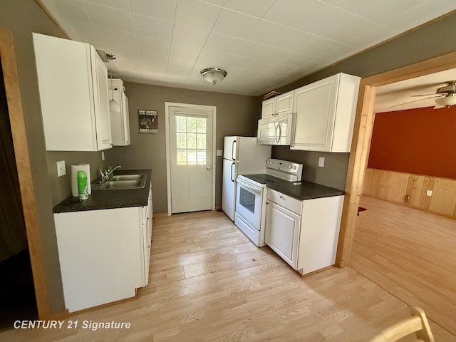 kitchen featuring white cabinetry, a sink, dark countertops, light wood-type flooring, and white appliances