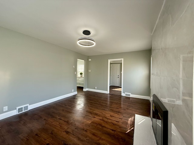 empty room featuring visible vents, baseboards, and dark wood-type flooring