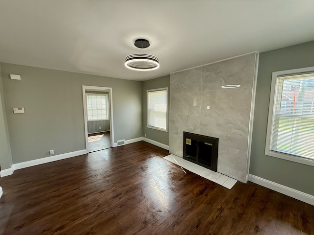 unfurnished living room with baseboards, dark wood-type flooring, and a tiled fireplace