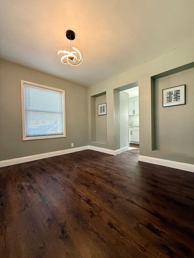 empty room with baseboards, a chandelier, and dark wood finished floors