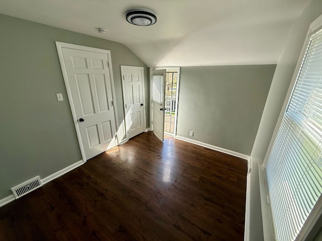 unfurnished bedroom with baseboards, lofted ceiling, wood finished floors, and visible vents