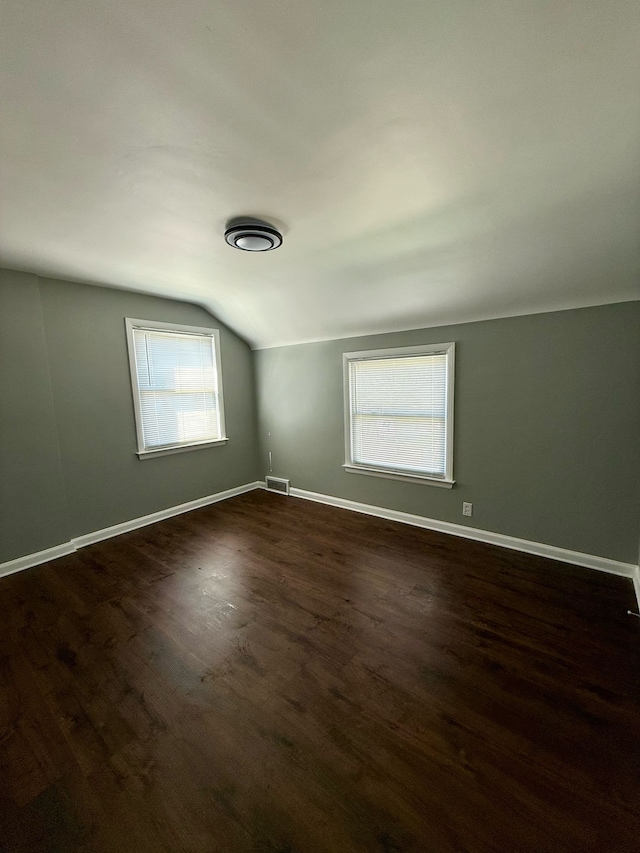 additional living space with baseboards, vaulted ceiling, dark wood-style floors, and visible vents