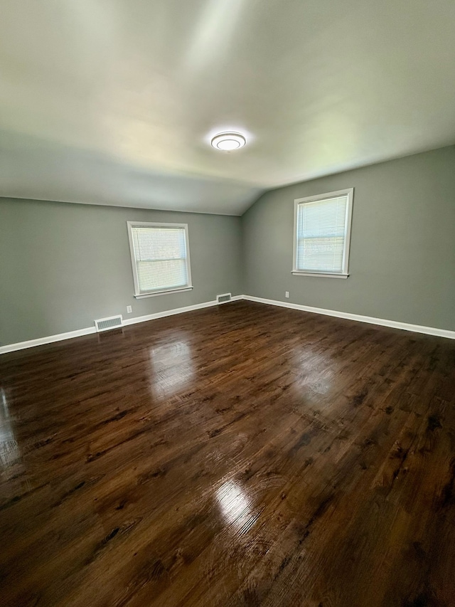 additional living space featuring visible vents, baseboards, dark wood-type flooring, and vaulted ceiling