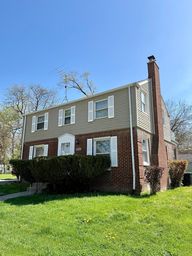 view of front of property featuring a chimney, a front yard, and brick siding