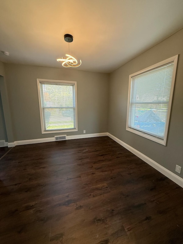 unfurnished dining area with a chandelier, visible vents, a wealth of natural light, and dark wood finished floors