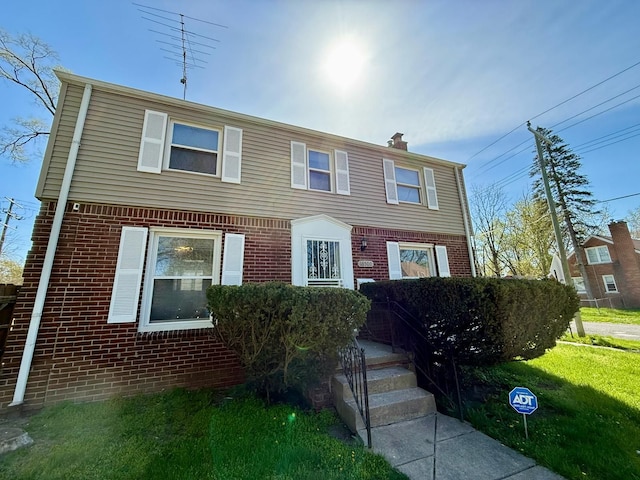 view of front of house featuring brick siding, a chimney, and a front yard