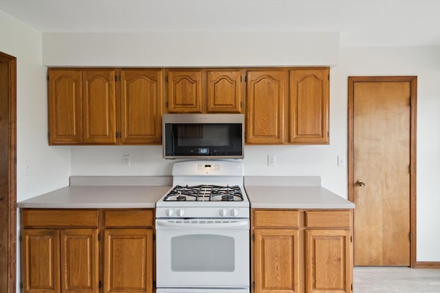 7996 Cain Rd, Jackson, MI 49201 - kitchen with stainless steel microwave, white range with gas cooktop, brown cabinets, and light countertops