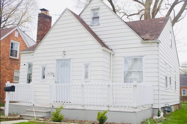 view of front of home with roof with shingles, a wooden deck, and a chimney