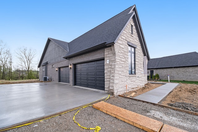 view of property exterior with roof with shingles, central AC unit, concrete driveway, an attached garage, and stone siding