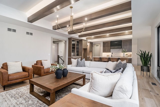 living area with a chandelier, visible vents, beam ceiling, and light wood-type flooring