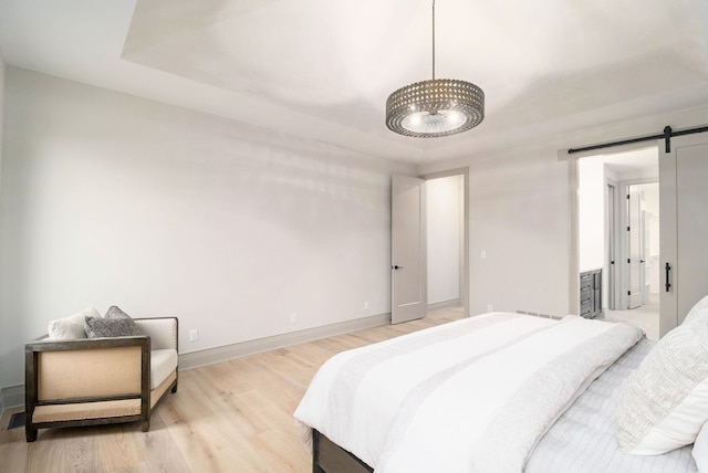 bedroom with a barn door, baseboards, a notable chandelier, a tray ceiling, and light wood-style flooring