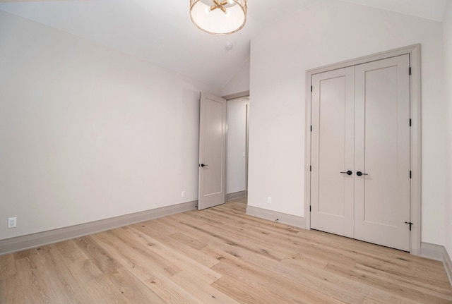 unfurnished bedroom with baseboards, a closet, light wood finished floors, and lofted ceiling