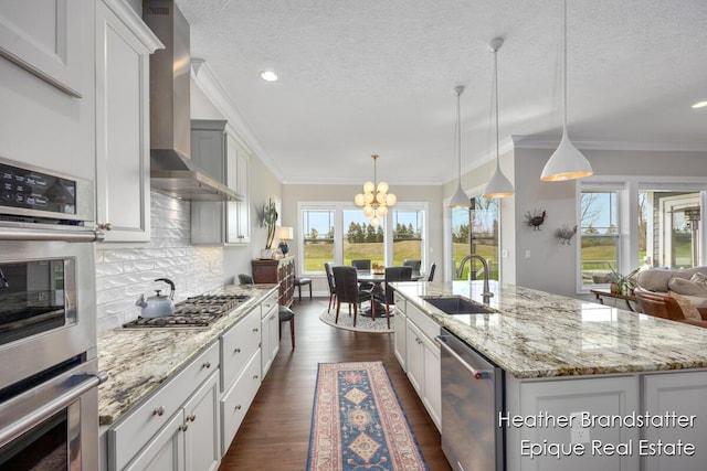 kitchen featuring appliances with stainless steel finishes, backsplash, a sink, a notable chandelier, and wall chimney exhaust hood