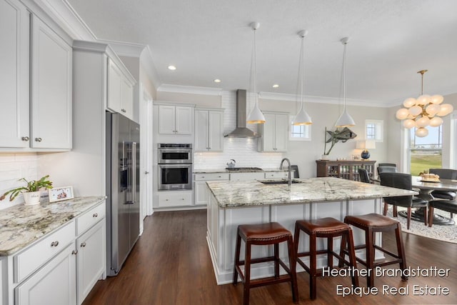 kitchen featuring a chandelier, appliances with stainless steel finishes, wall chimney range hood, ornamental molding, and a sink