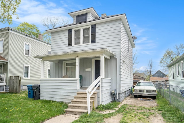 american foursquare style home featuring a porch, a front yard, board and batten siding, and fence
