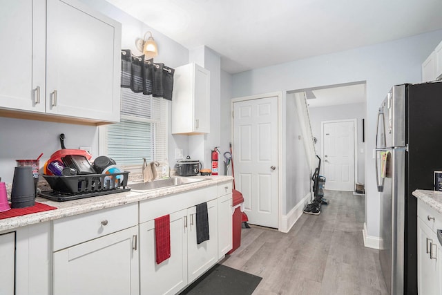 kitchen featuring light wood finished floors, a sink, baseboards, white cabinets, and freestanding refrigerator