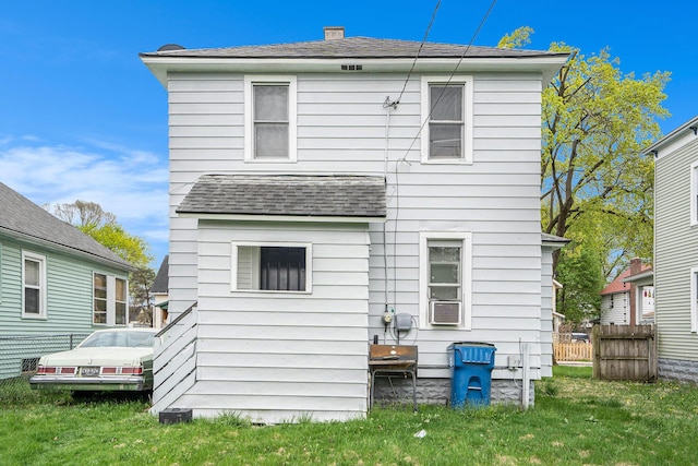 rear view of property featuring fence, roof with shingles, and a lawn