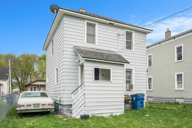 rear view of house with cooling unit, a chimney, a yard, and a shingled roof