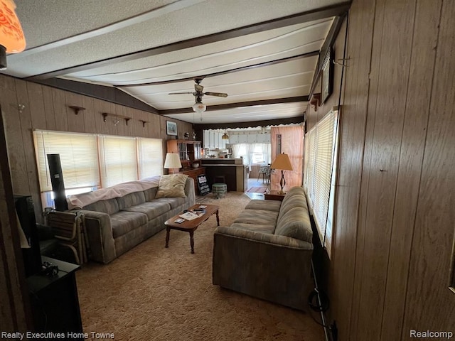 carpeted living area featuring a ceiling fan, wood walls, and vaulted ceiling with beams