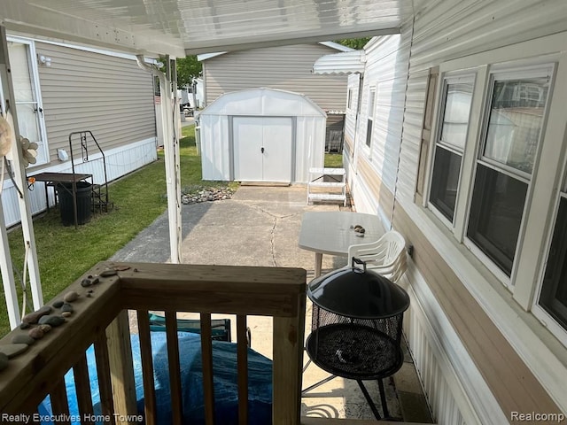 wooden terrace featuring a lawn, a storage unit, a patio, and an outbuilding