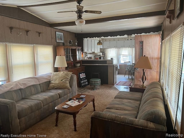 living room with carpet flooring, a ceiling fan, wooden walls, and beamed ceiling