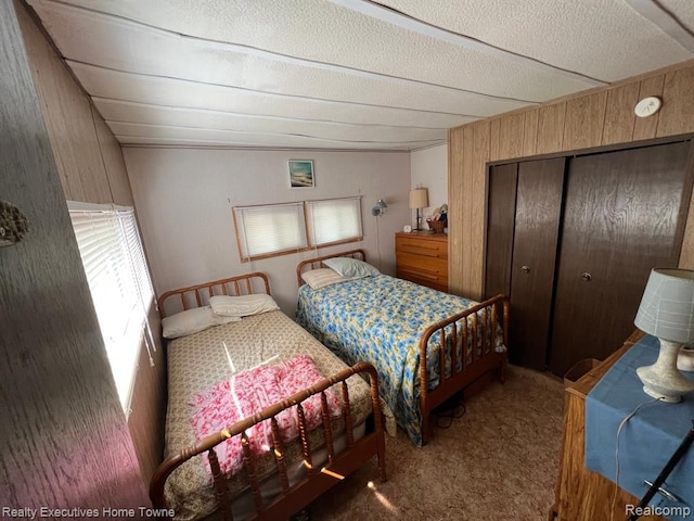 carpeted bedroom featuring a closet, wood walls, and a textured ceiling