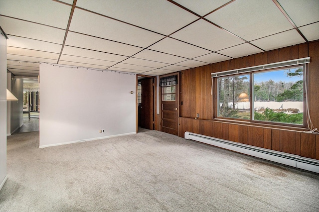 carpeted spare room featuring baseboards, wood walls, a paneled ceiling, and a baseboard radiator