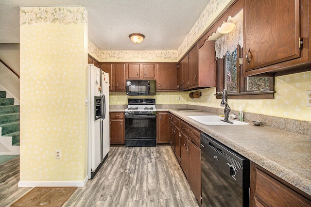 kitchen featuring wallpapered walls, light countertops, black appliances, a sink, and light wood-type flooring