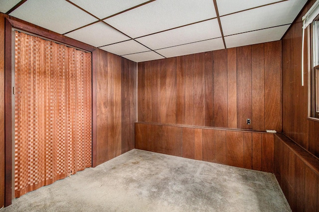 carpeted empty room featuring wooden walls and a paneled ceiling
